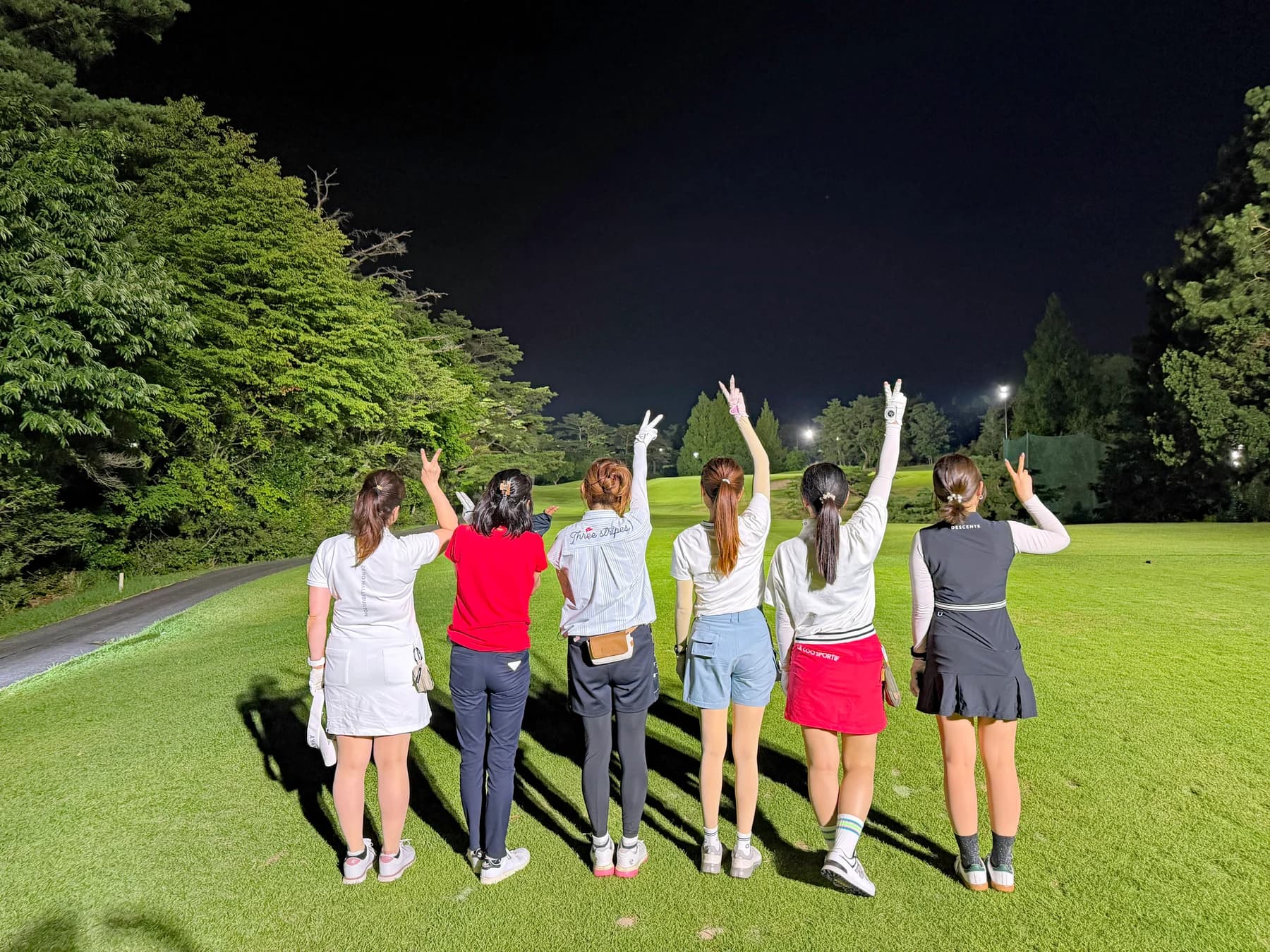 ナイトゴルフのコースで、6人の女性メンバーが後ろ向きに手を上げている
